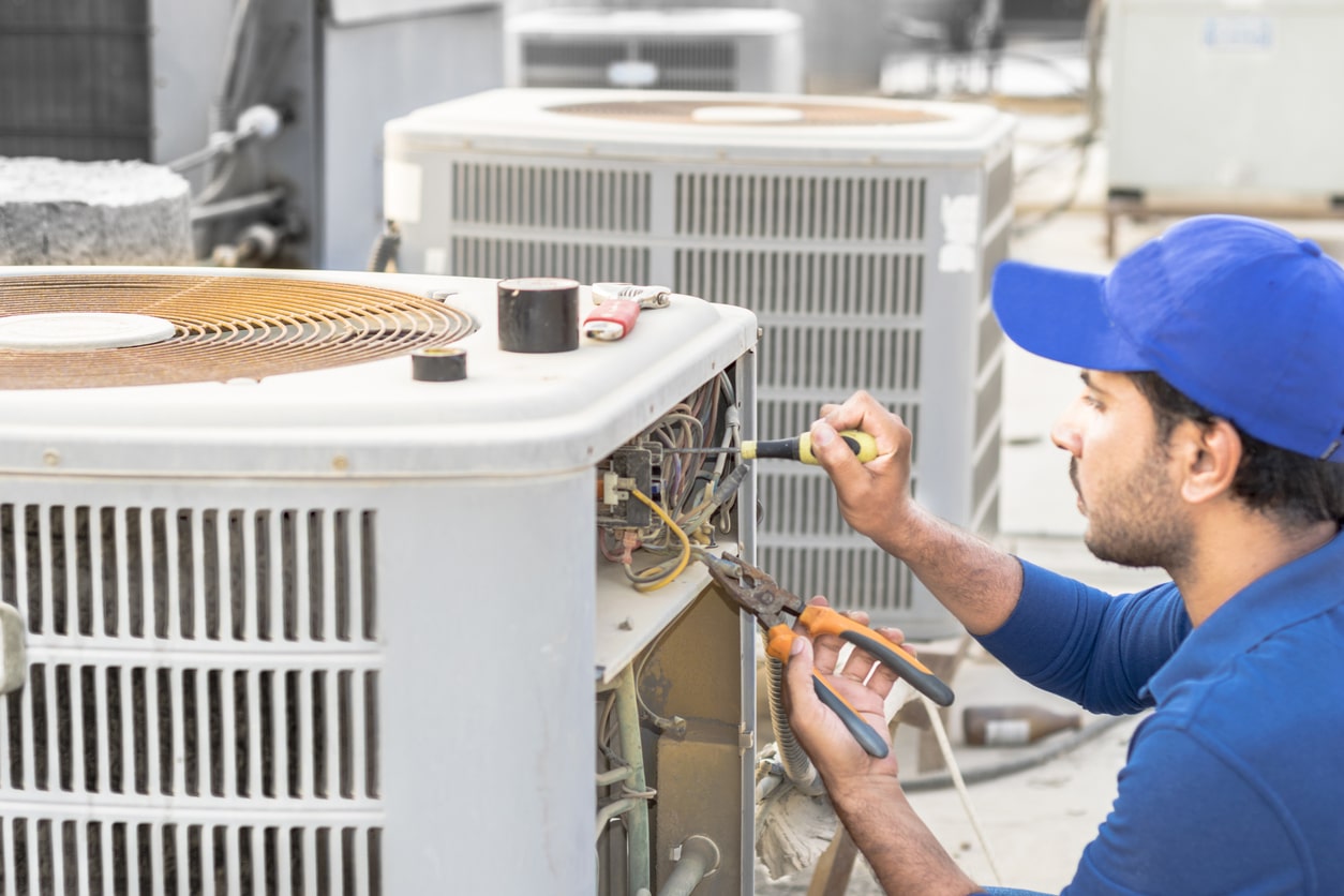 a professional electrician man is fixing the heavy unit of an air conditioner at the roof top of a building and wearing blue uniform and head cap